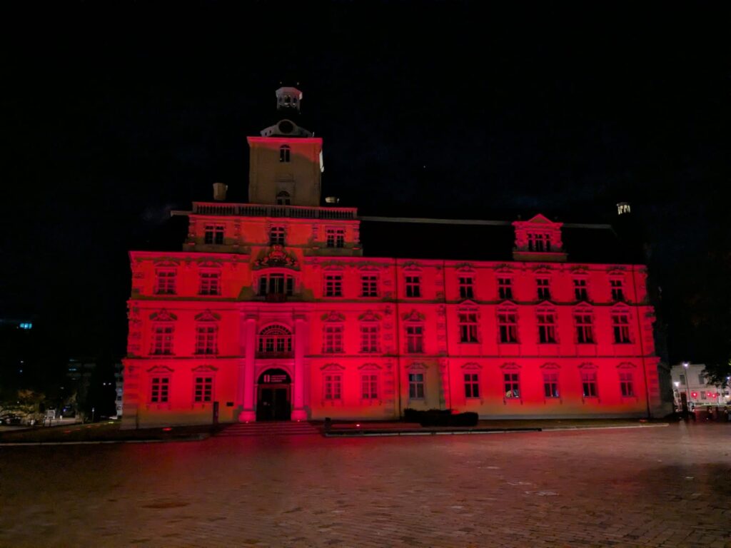 Ein historisches mehrstöckiges Gebäude bei Nacht, beleuchtet von leuchtend roten Scheinwerfern.